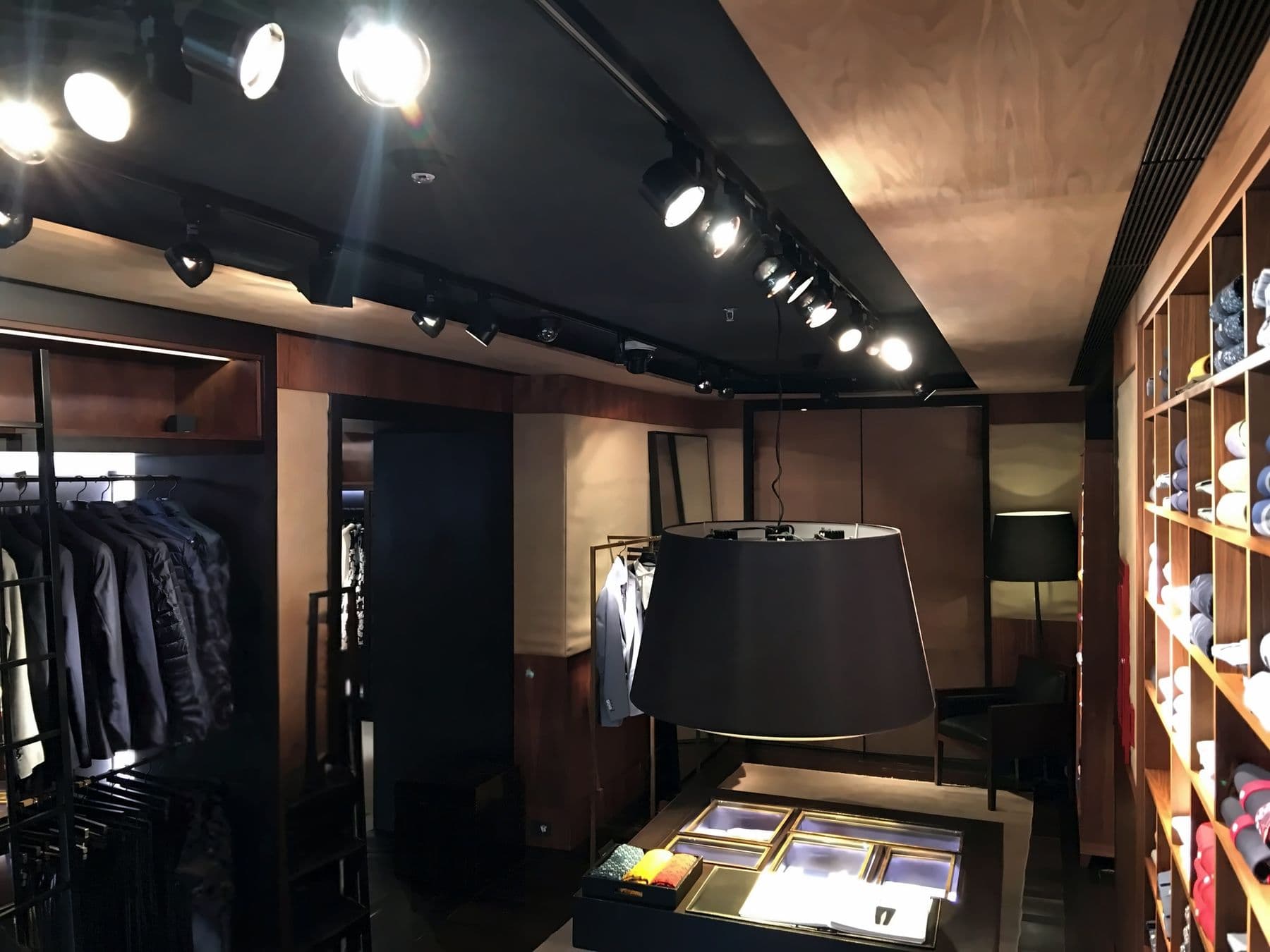 Interior de la boutique Carolina Herrera: focos de riel sobre el techo negro, percheros con trajes y mesa de exhibición iluminada