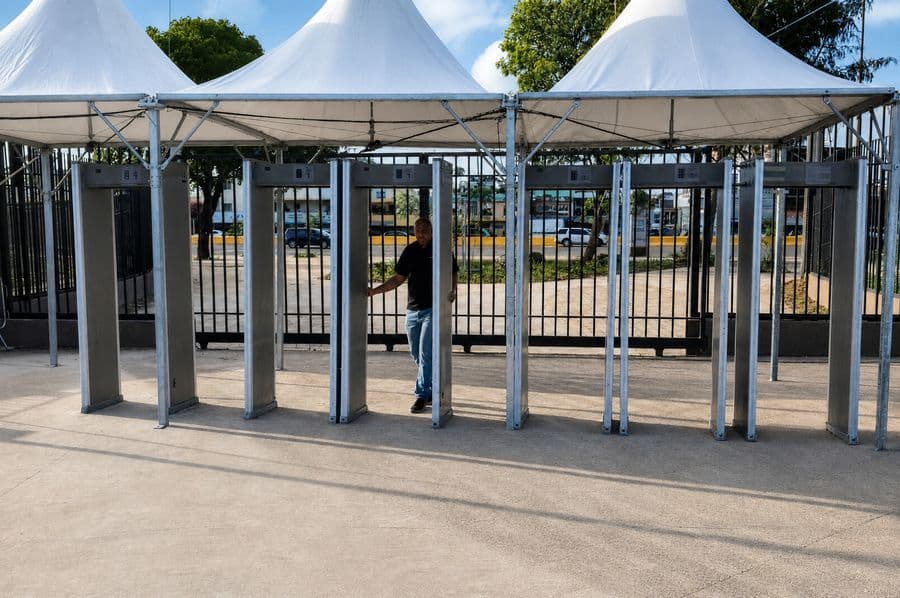 Siete arcos detectores de control de acceso alineados bajo carpas blancas en un acceso exterior de los Juegos 2026