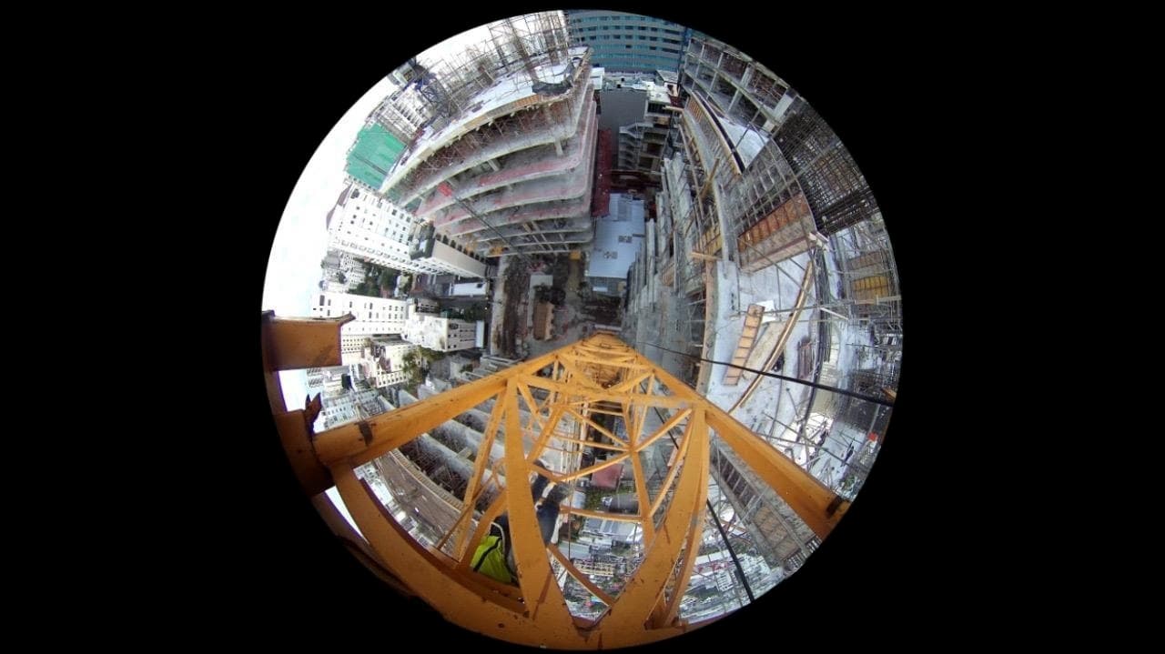 Vista ojo de pez desde la cámara instalada en lo alto de una grúa de obra, con la estructura amarilla, el técnico y los edificios en construcción