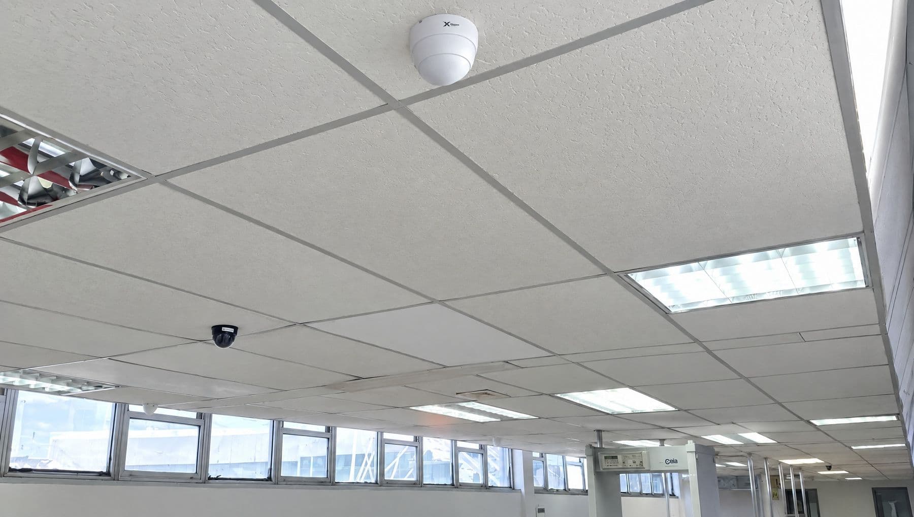 Cámara domo blanca montada en techo modular de la terminal, con arco detector al fondo