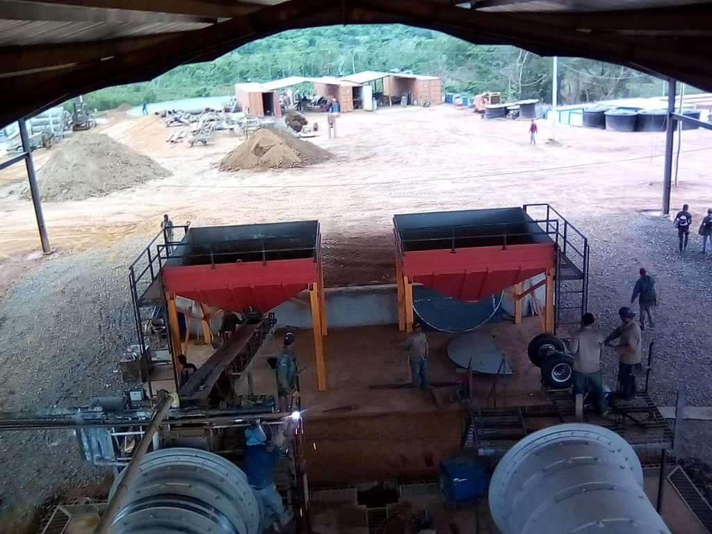 Nave de proceso de una planta minera en construcción con tolvas rojas y tambores cilíndricos, vista desde altura