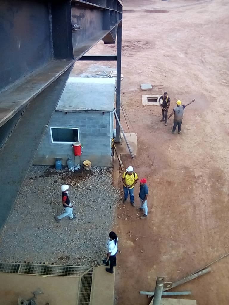 Trabajadores con casco junto a una caseta de bloques y una viga metálica en una planta minera en obra