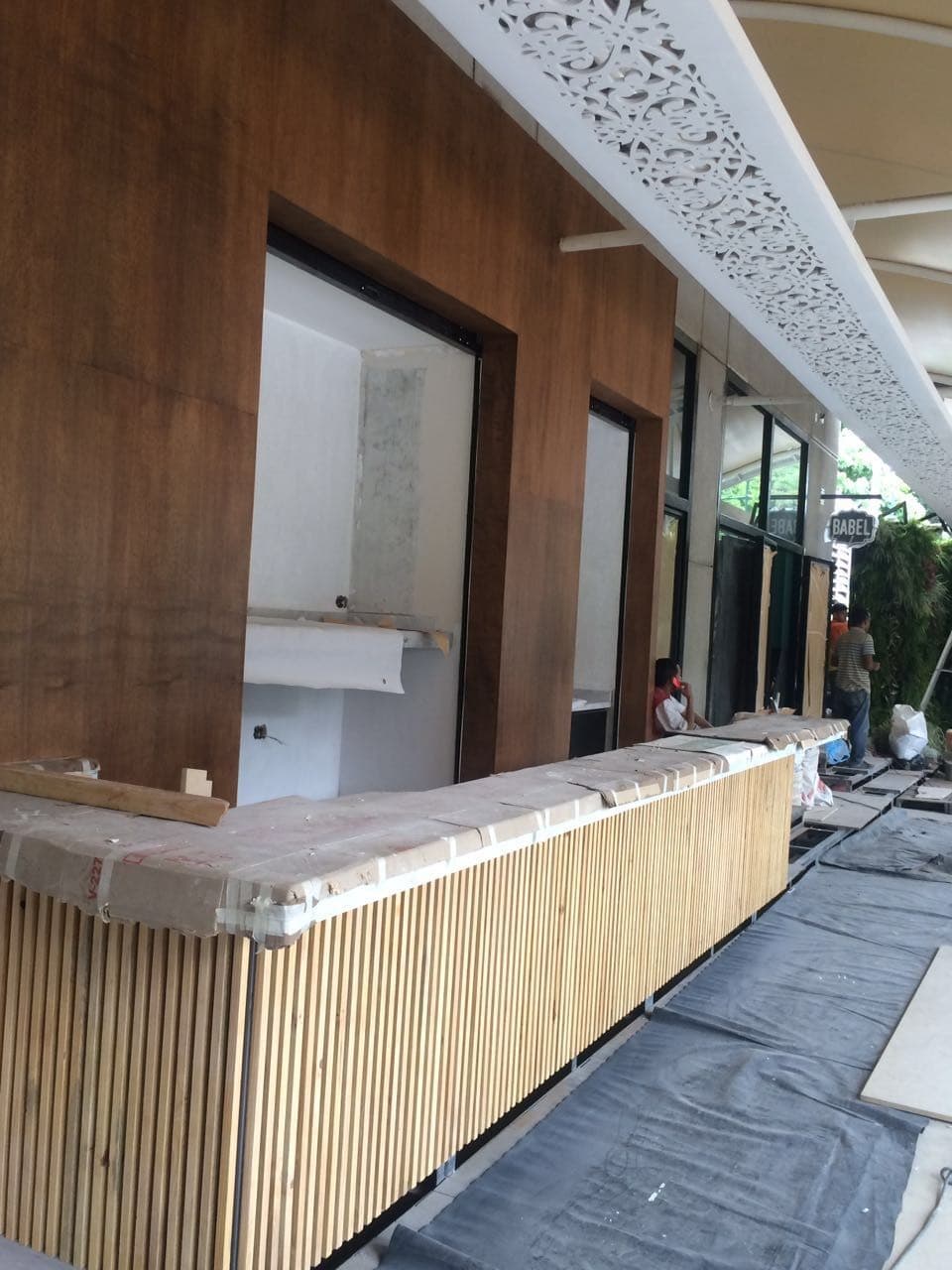 Fachada en obra del restaurante Babel con barra de madera protegida, revestimiento de madera y celosía blanca en el techo