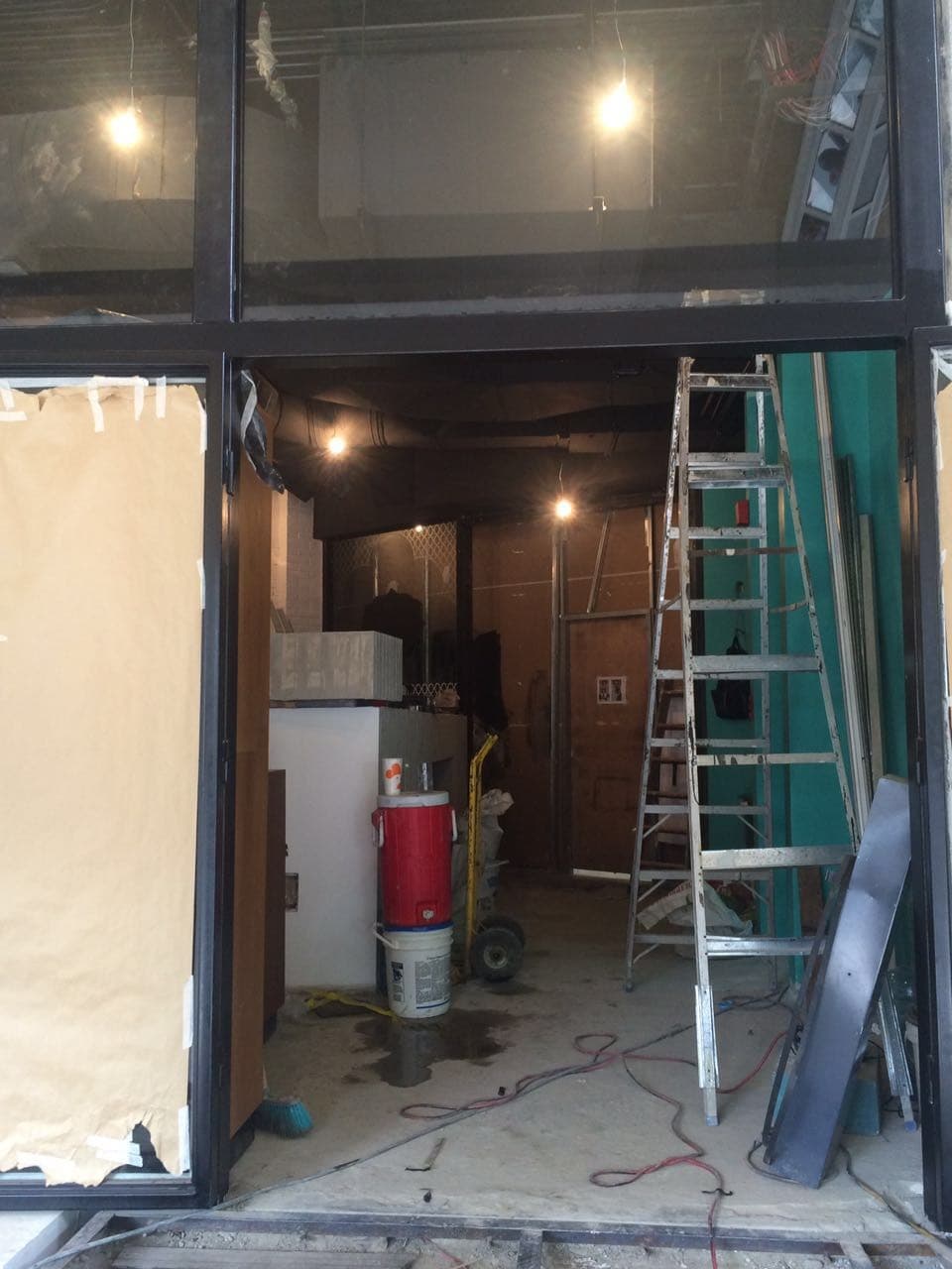 Interior del local en obra con escalera, cableado en el techo y puertas protegidas con papel